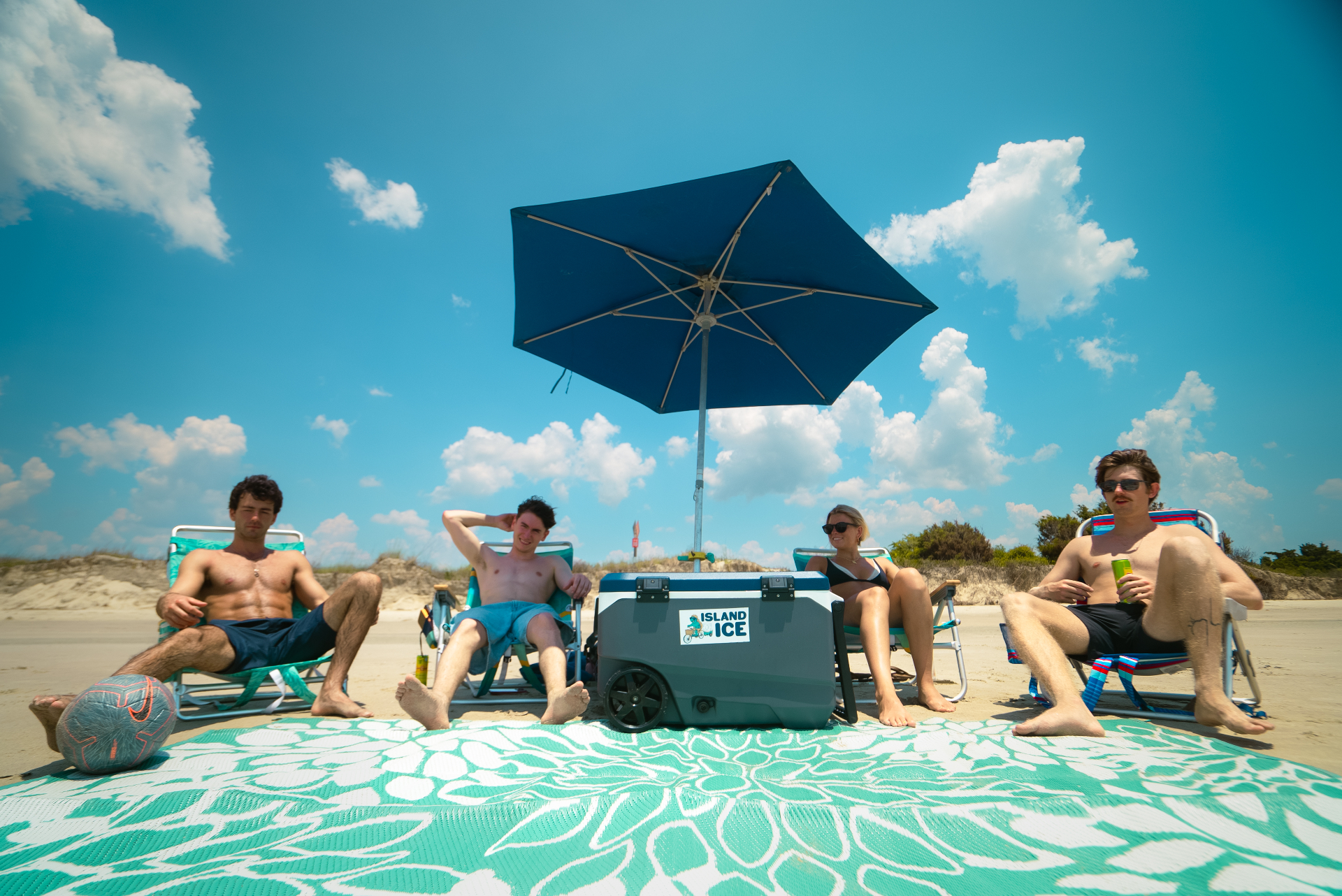 Friends relaxing on the beach with an Island Ice cooler under a blue umbrella